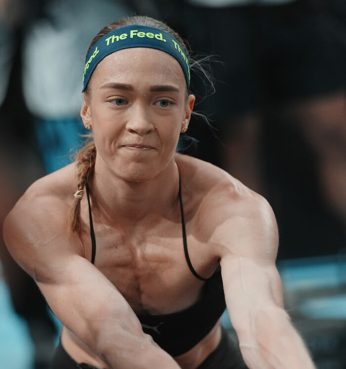 Close-up of a determined HYROX athlete mid-race, showcasing her intense focus and muscular physique.