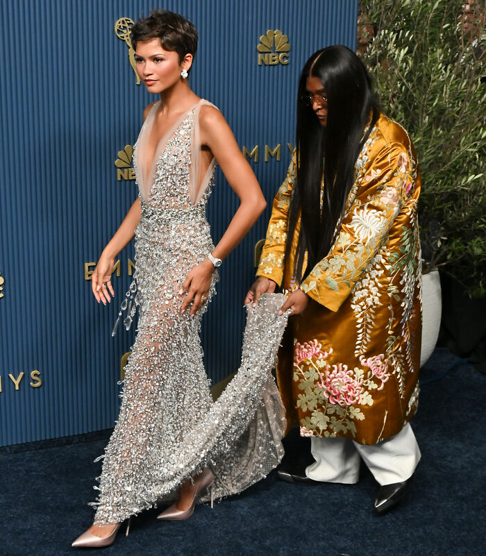Zendaya's stylist helping her with the gown on the red carpet, a moment sparking intense scrutiny.