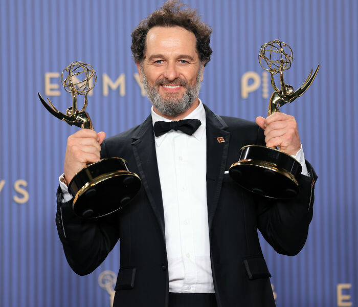 Emmy Winner beaming, holding two Emmy awards, looking tense with wife.