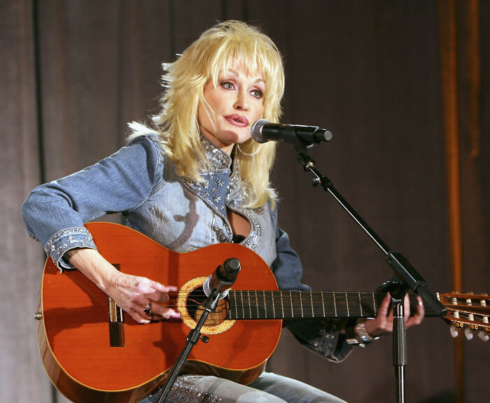 Dolly Parton singing into a microphone while playing an acoustic guitar Dolly Parton singing into a microphone while playing an acoustic guitar