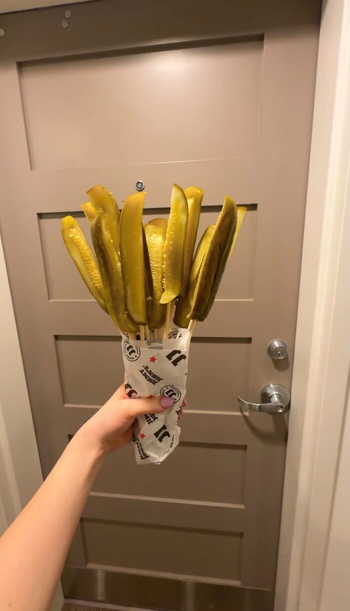 A hand holding a bouquet of pickles wrapped in paper, an unhinged image.