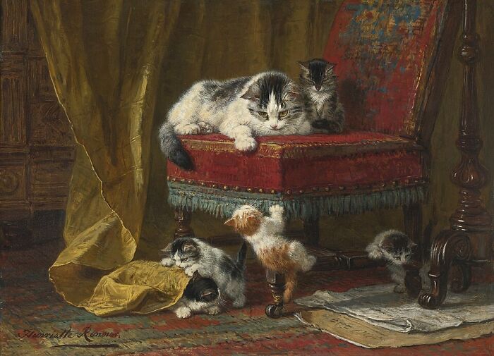 A 19th-century cat painting of a mother cat and her kittens playing on and around a red velvet chair. This cat painting evokes domestic warmth.