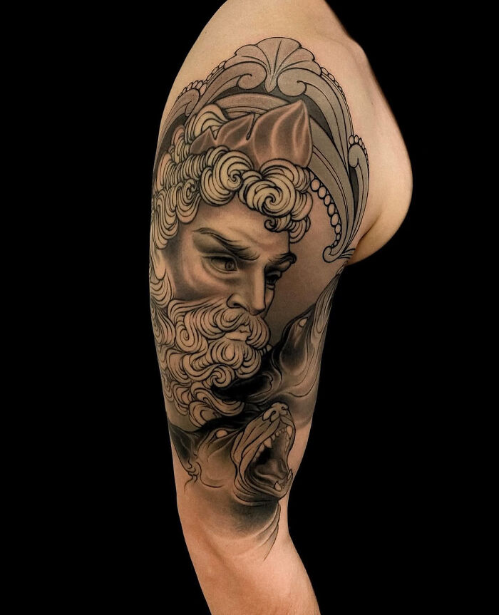 Stunning mythology tattoo of a sculpted mans head on a bicep, from Sacred Gold Studio.