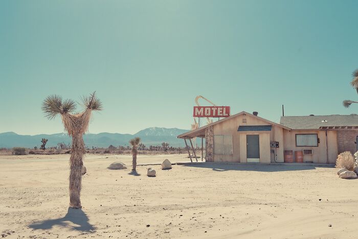 A wide shot of a dusty motel in the American West, showcasing rusty remnants of a bygone era under clear skies.