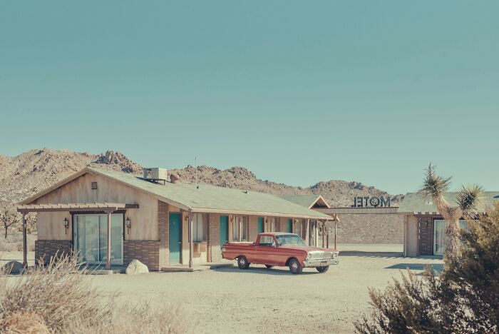 A vintage red truck parked in front of a rustic motel, exploring the bygone American West.
