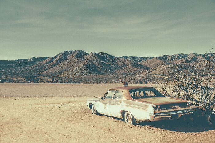 A rusty, old police car is parked in a barren landscape with mountains in the background in the American West. Rusty and dusty remnants.