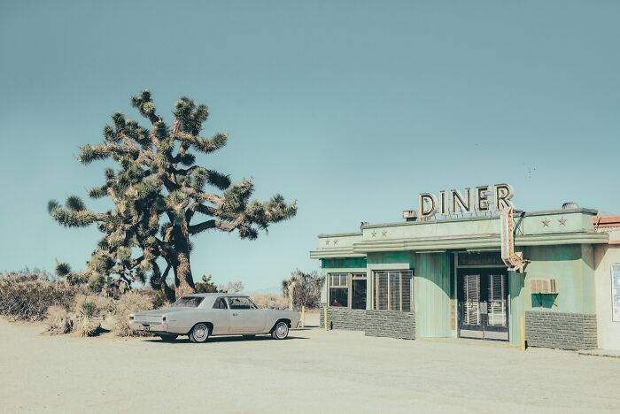 A photographer captures a classic car in front of a rustic diner, remnants of the bygone American West.
