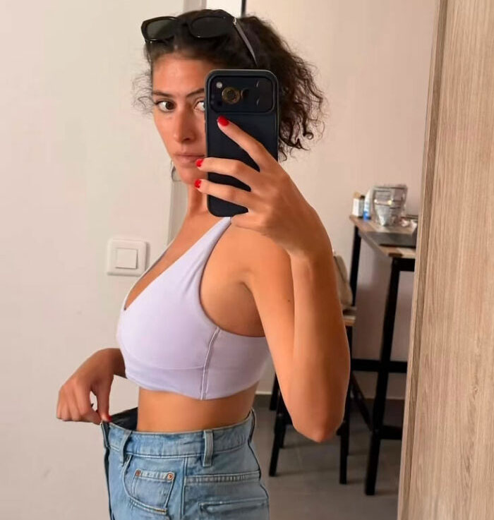 Woman showing loose jeans, reflecting body image issues often linked to Western beauty standards. Woman showing loose jeans, reflecting body image issues often linked to Western beauty standards.