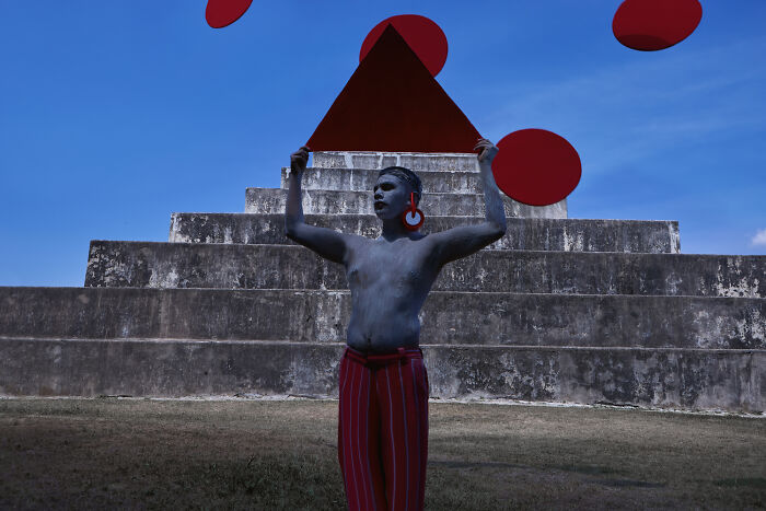 Surreal art photo of person painted gray holding red triangle with red circles against blue sky