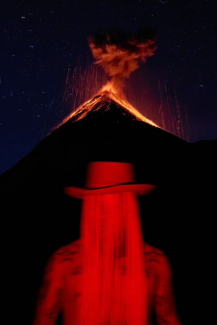 Surreal art expedition photo of red glowing figure with long hair silhouette against erupting volcano