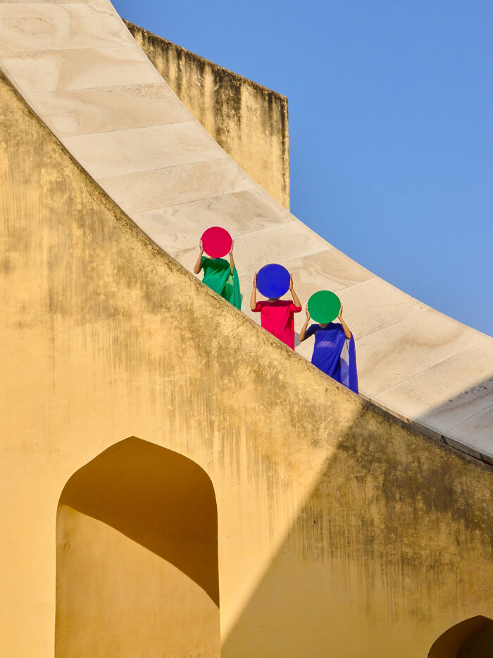 Surreal art expedition photo of three women with colorful discs on yellow curved architectural structure