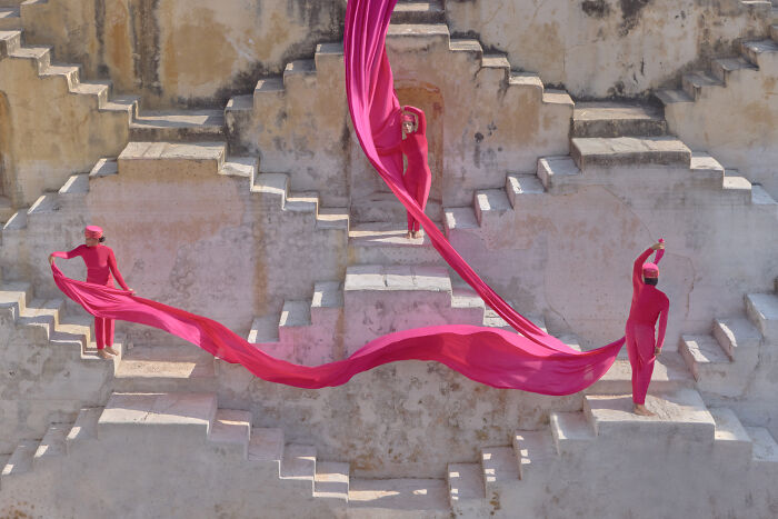 Surreal photo of three people dressed in pink with flowing fabric on stepped architecture