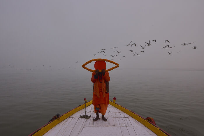 Person on boat holding orange eye-shaped object with birds flying in misty background