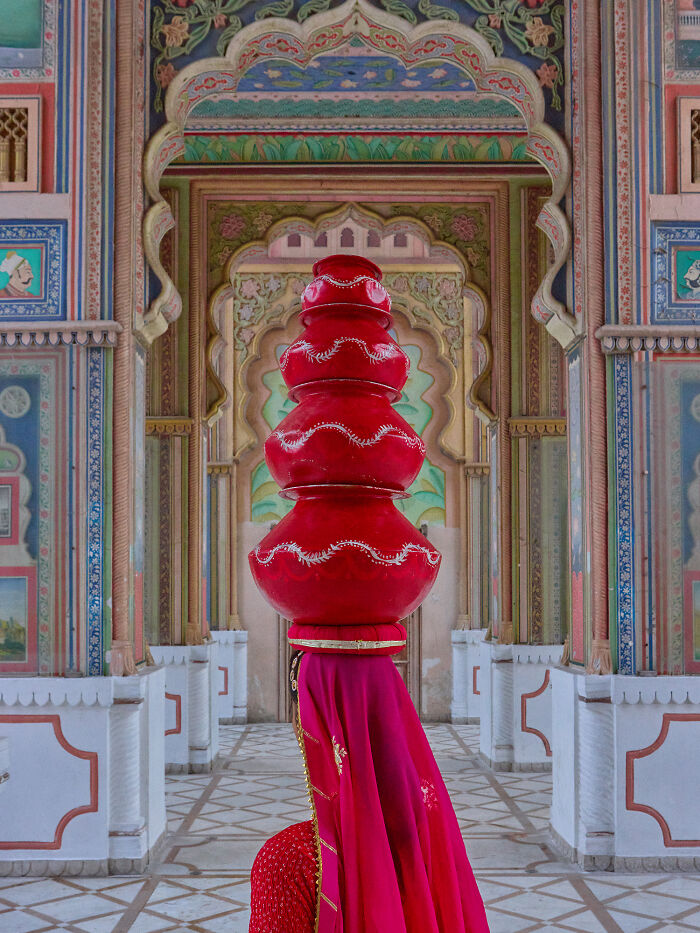 Surreal photo of woman balancing large red pots in colorful ornate hallway
