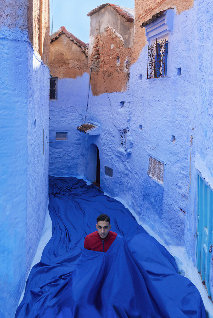Man standing in surreal blue alley with flowing blue fabric blending into walls