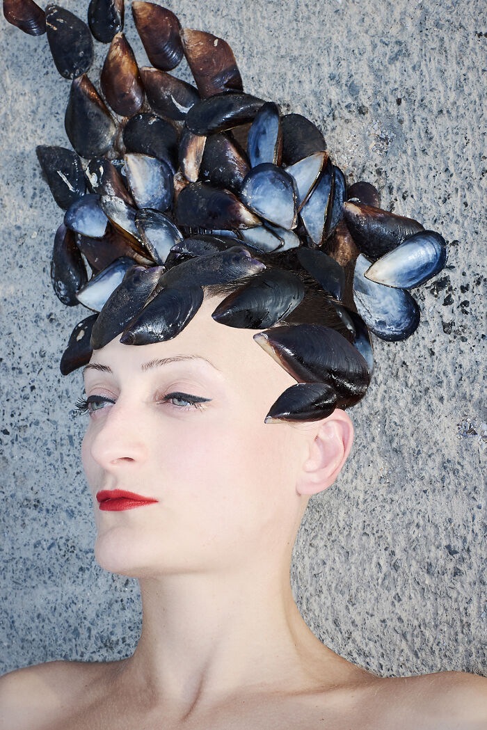 Surreal photo of woman with mussels arranged on head like hair against stone background