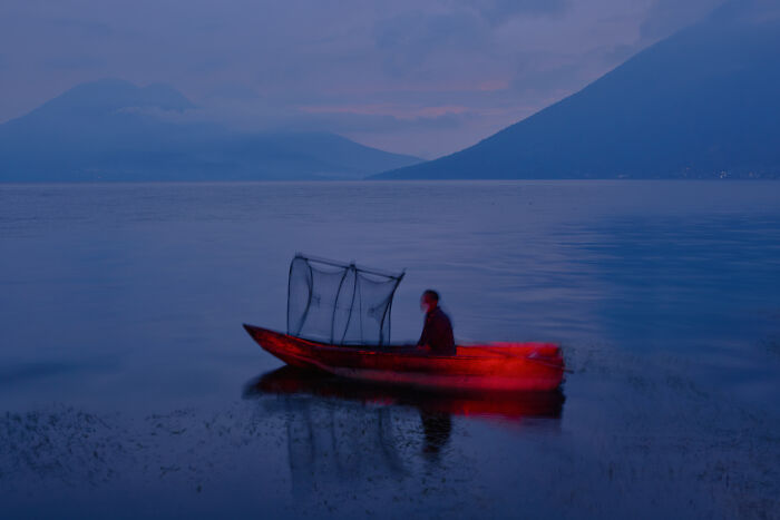Surreal photo of person in red boat on lake with misty mountains in background