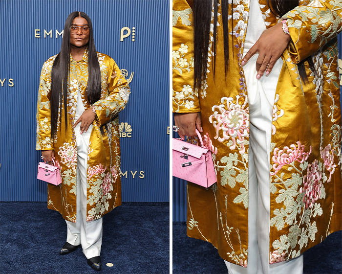 A star in a worst dressed outfit at the 2026 Emmys, in a long, gold, embroidered coat over white pants, holding a tiny pink bag.