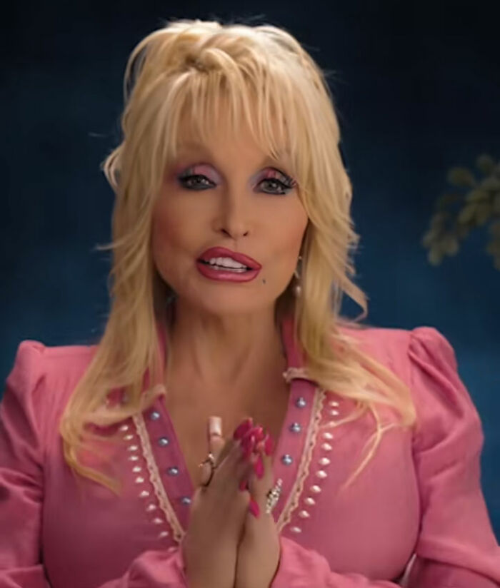 Dolly Parton in a final video, wearing a pink top, hands clasped, looking at the camera. Dolly Parton in a final video, wearing a pink top, hands clasped, looking at the camera.