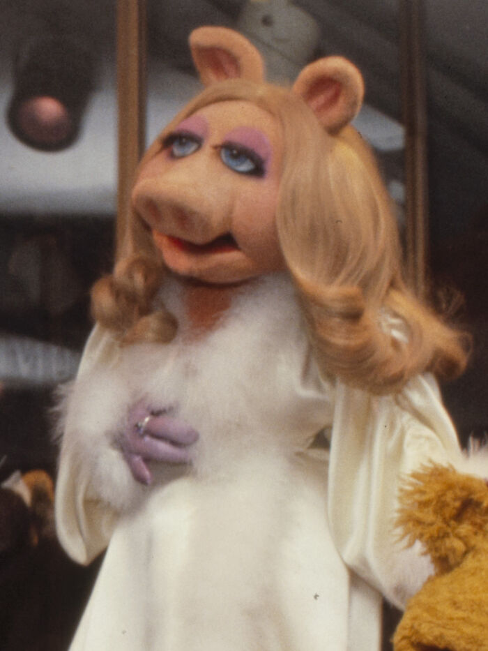 Miss Piggy in a white dress with a fur collar, enjoying a delicious dinner and hot tea.