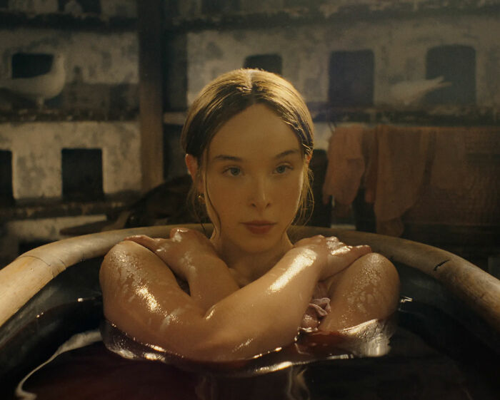A scene from the Lizzie Borden series showing a young woman bathed in a dark wooden tub with arms crossed. A scene from the Lizzie Borden series showing a young woman bathed in a dark wooden tub with arms crossed.