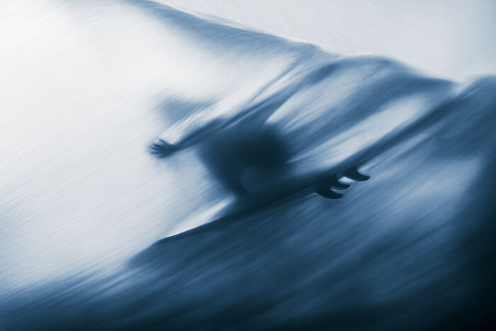 A blurred image of a manta ray swimming gracefully through blue water, an Ocean Photographer of the Year image.