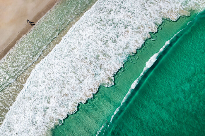 Aerial view of turquoise ocean waves crashing on a sandy beach, a beautiful image from the Ocean Photographer Awards.