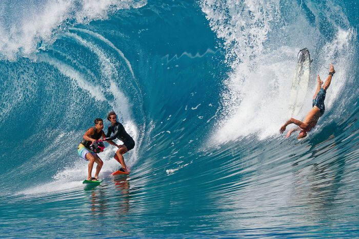 Two surfers on a large ocean wave, with another surfer falling off his board, an Ocean Photographer of the Year image.