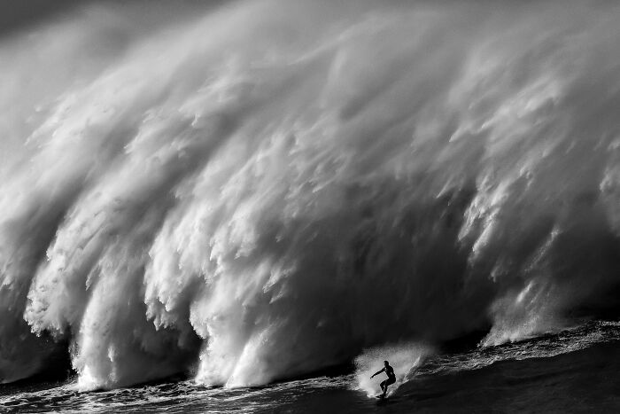 A lone surfer rides a massive ocean wave in black and white, one of the stunning images from the Ocean Photographer of the Year Awards.