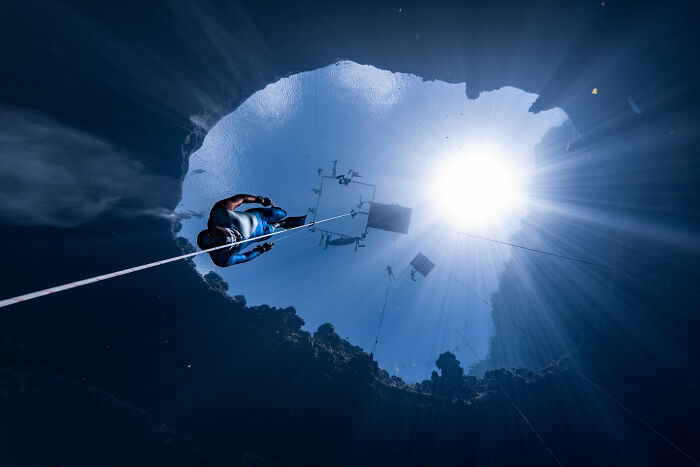 A freediver descends into a blue hole from below, capturing stunning images for the Ocean Photographer of the Year Awards.