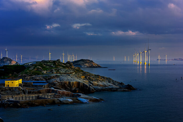 Wind turbines reflecting on the ocean at dusk, a stunning image from the Ocean Photographer of the Year Awards.