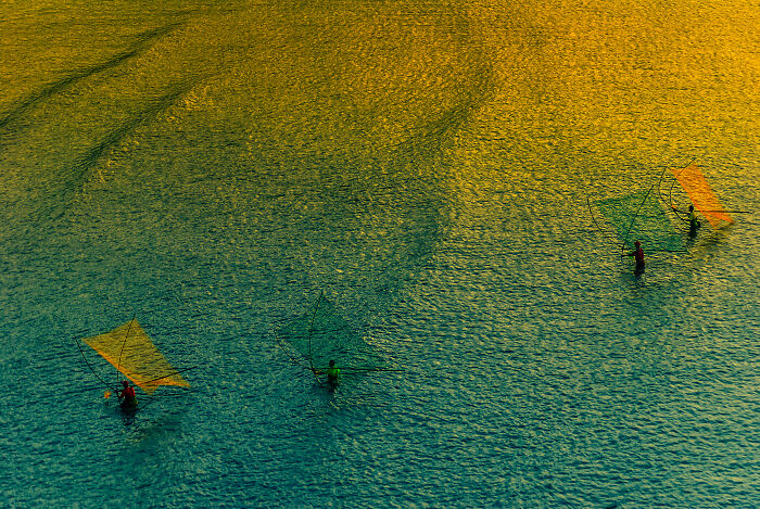 Three people in calm water with colorful fishing nets, capturing a moment for the Ocean Photographer Awards.