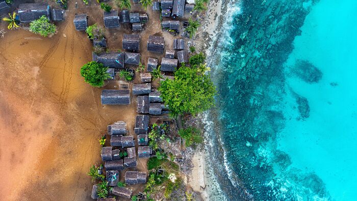 An aerial view of a coastal village with homes on land beside the stunning blue ocean, from the Ocean Photographer Awards.