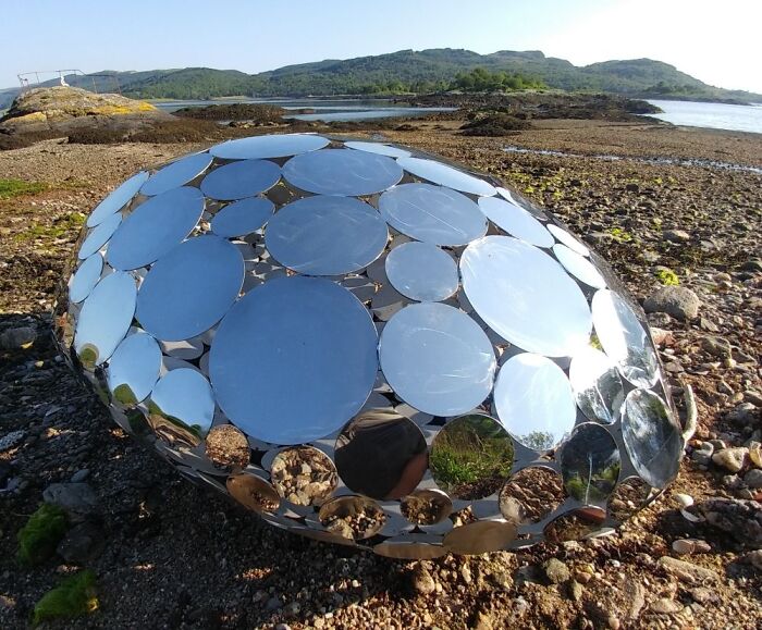 Reflective sculpture made of circular mirrors resting in a woodland stream