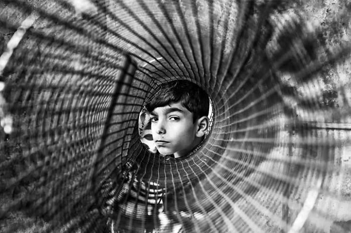 A black and white street photo by Murat Harmanlikli highlighting the curiosity of childhood with a boy inside a spiral.