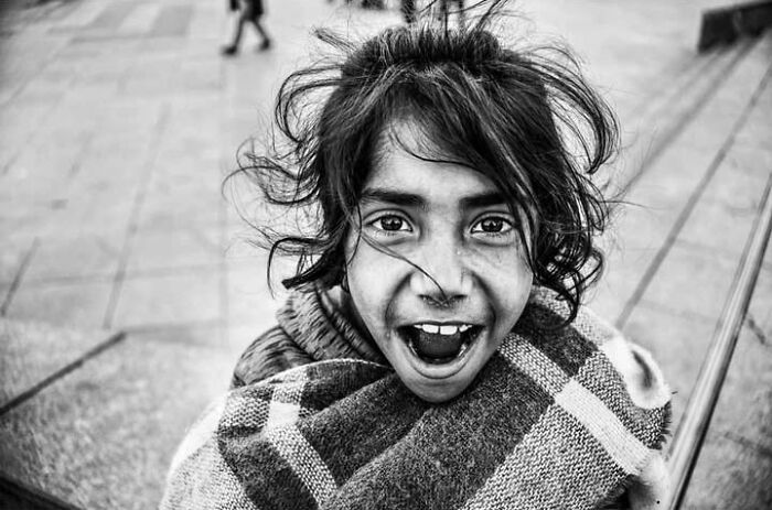 A black and white street photo by Murat Harmanlikli capturing the joy of childhood with a girl's wide smile.
