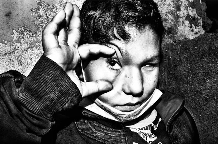 A Murat Harmanlikli street photo capturing the curiosity and intensity of childhood, with a boy pulling at his eye.