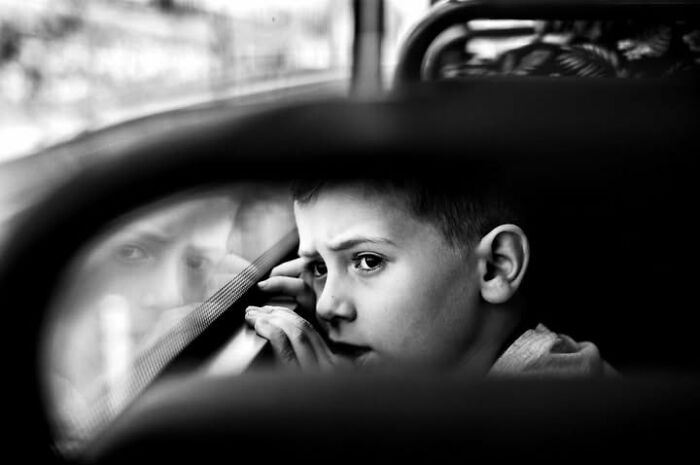 A Murat Harmanlikli street photo of a child looking out a window with a pensive gaze, reflecting the intensity of childhood.