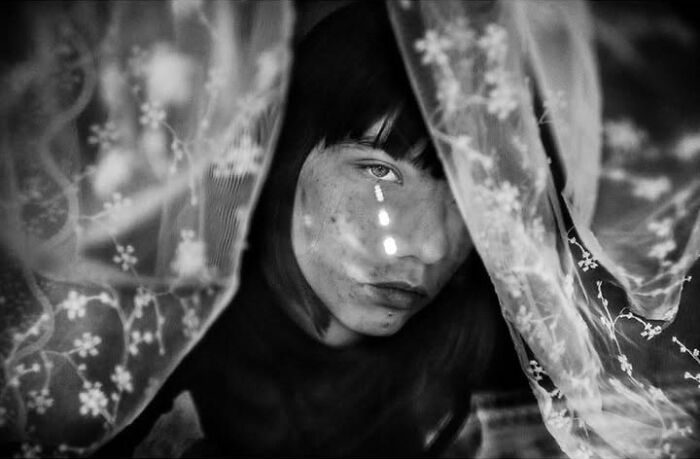 Murat Harmanlikli captures a child's intense expression through a curtain in a street photo, highlighting childhood.