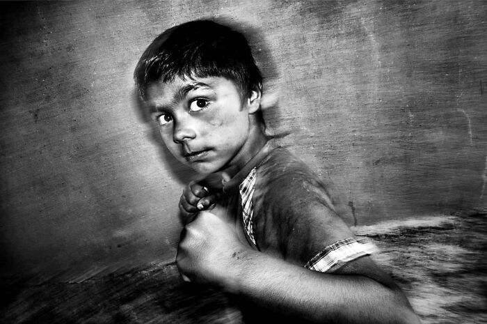 A black and white street photo showing the curiosity and intensity of childhood, featuring a young boy with dirt on his face, hands clenched.
