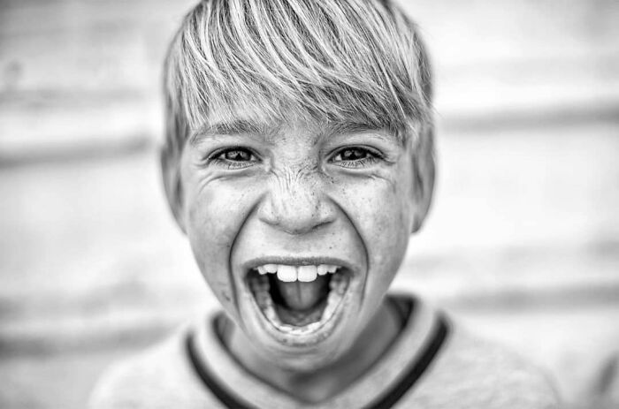 A black and white street photo captures the joy and intensity of childhood, featuring a young boy with his mouth wide open, mid-scream.