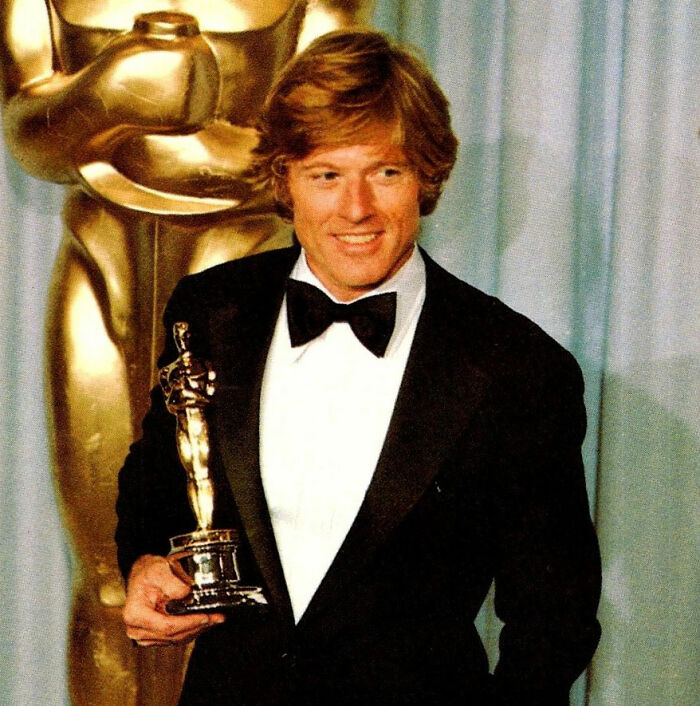 Robert Redford, a celebrity, holding an Oscar award with a golden statue in the background, showing hot takes.