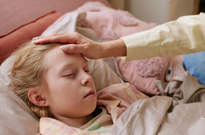 A child sleeping in bed, with an adult hand on their forehead, showing signs of sickness.
