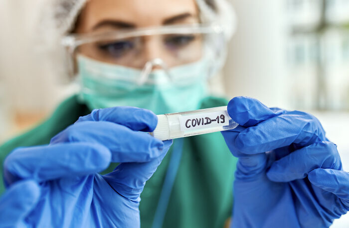 A medical professional in PPE holding a COVID-19 test tube, related to extreme illness and sickness.
