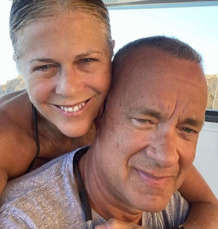 Tom Hanks, a celebrity, smiling as a woman embraces him from behind, showcasing brutal hot takes.