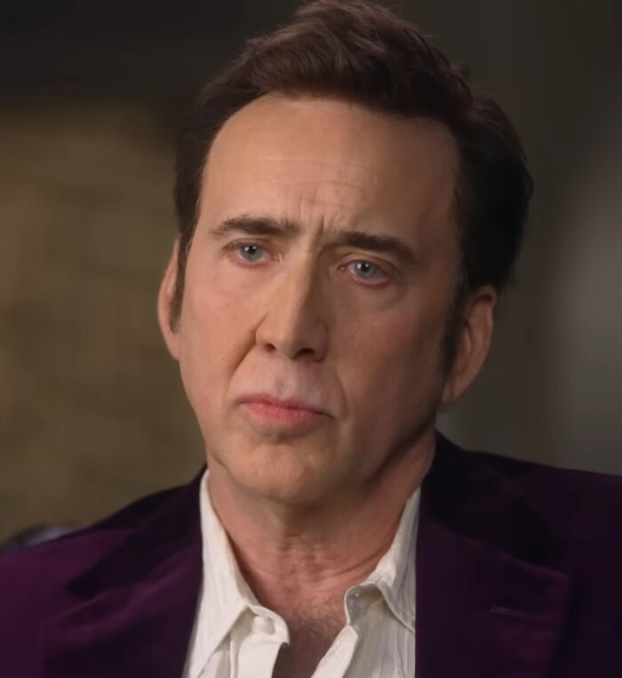 Nicolas Cage in a purple velvet jacket, looking thoughtful, ideal for articles about celebrity hot takes.
