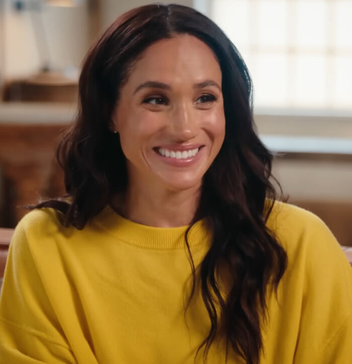Meghan Markle smiling in a yellow sweater, sharing her brutal hot take on celebrities.