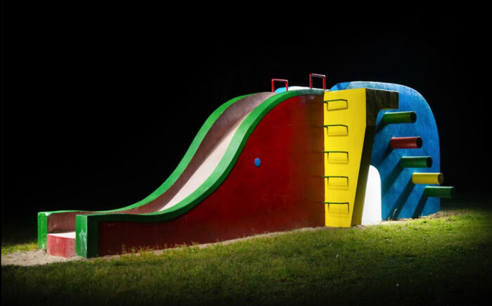 A colorful, surreal Japanese playground at night with a multi-colored slide and climbing structure, by Fujio Kito.