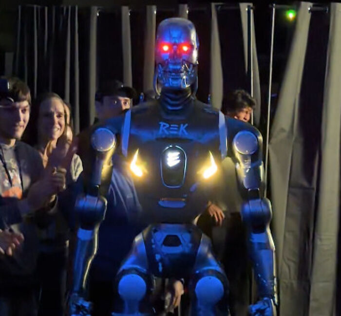 Robot with glowing red eyes entering arena amidst crowd