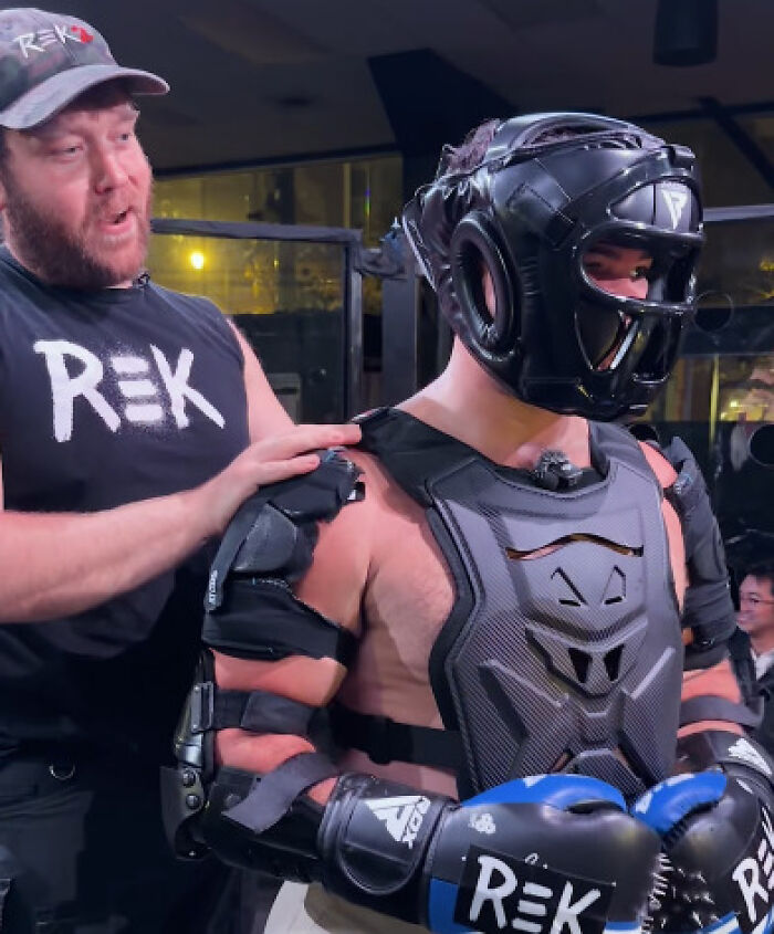 Trainer helping fighter in protective gear prepare for man vs robot cage fight